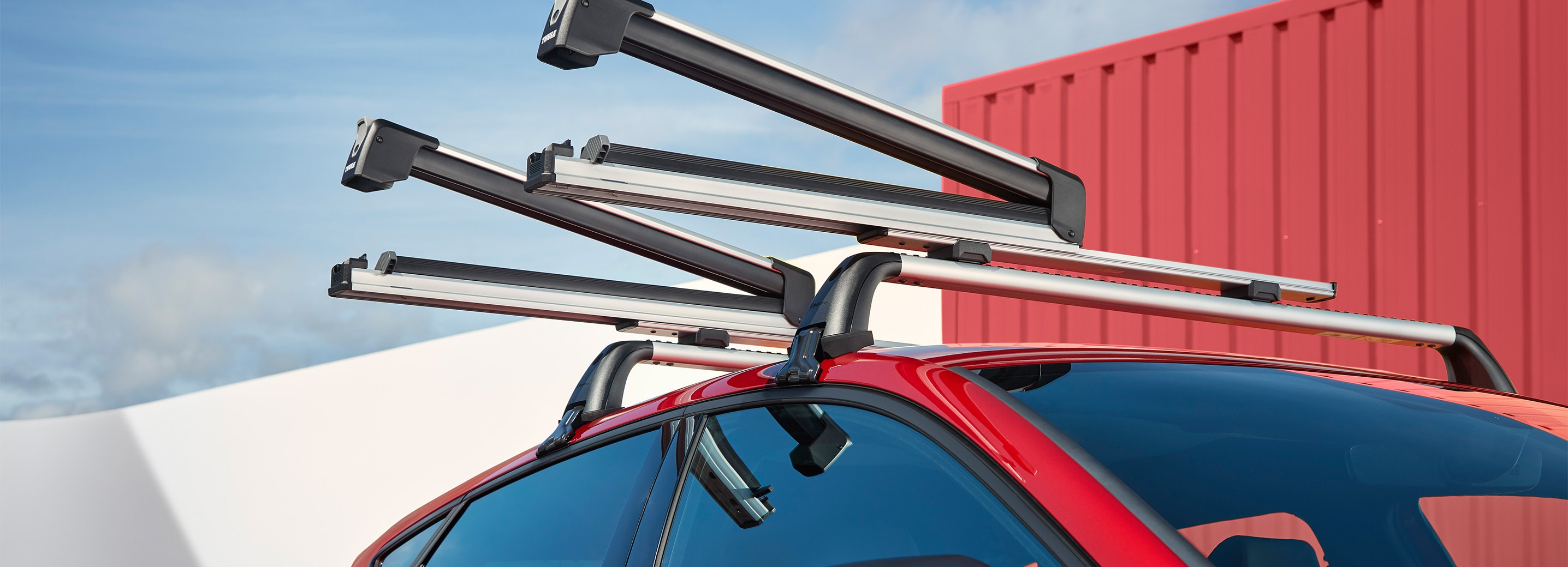 A red SEAT Leon parked in a snowy mountain landscape with two people securing skis to the roof rack and another person standing by the open door.