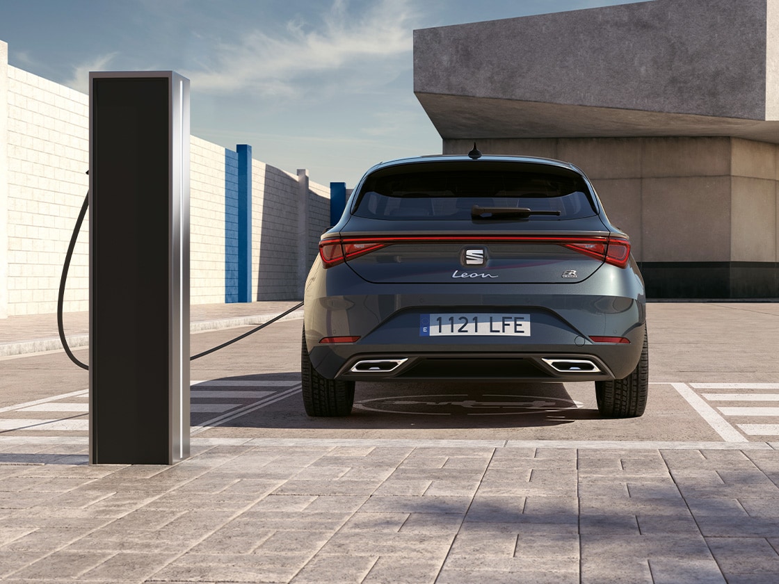 Rear view of the seat leon fr automatic car charging at a station, a new hatchback for 2025 in magnetic grey, complete with rear parking sensors and led headlights and taillights.