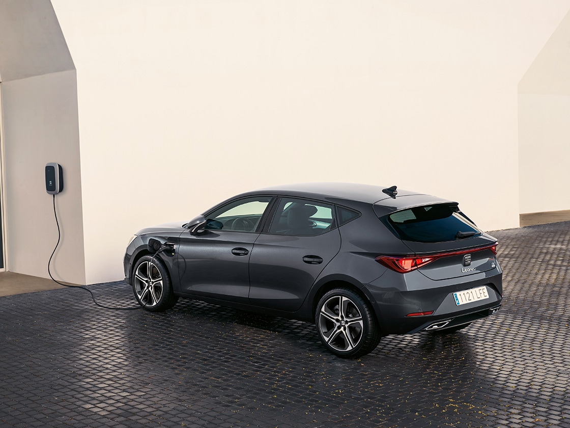 SEAT Leon hatchback 2025 plug in hybrid electric vehicle. Parked and charging outdoors, featuring spoke alloy wheels, interior ambient lighting and heated front seats for optimal comfort.