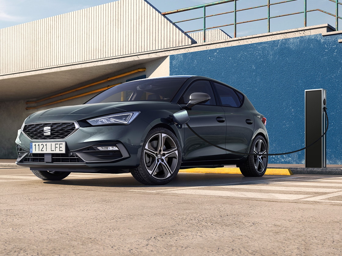 The seat leon e hybrid, a hybrid electric car, parked near a charging station, showcasing the e manager feature for impressive value.