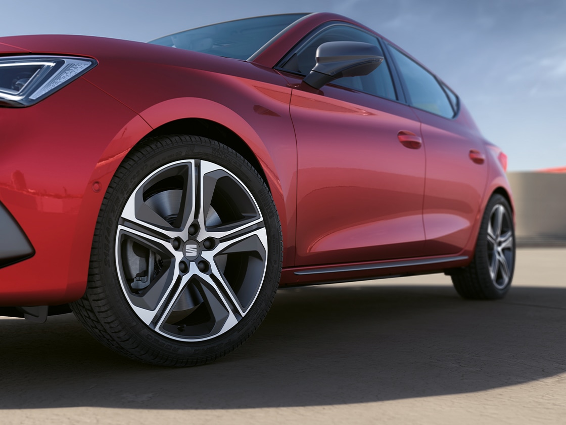 A desire red seat leon focusing on the side door moulding and alloy wheel, with the car parked under a clear sky.