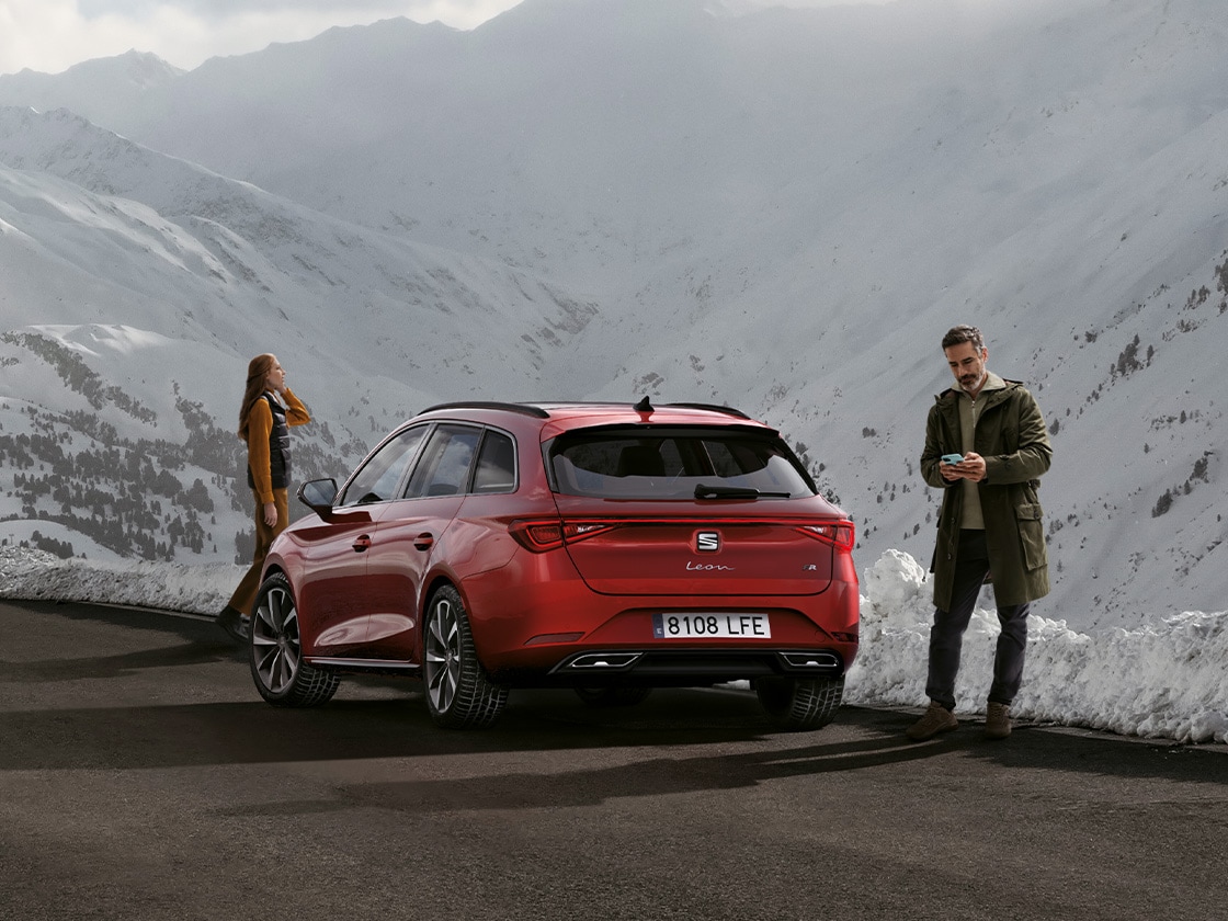 A red seat leon car parked on a mountain road waiting for seat service mobility and roadside assistance benefits. Two people standing nearby.