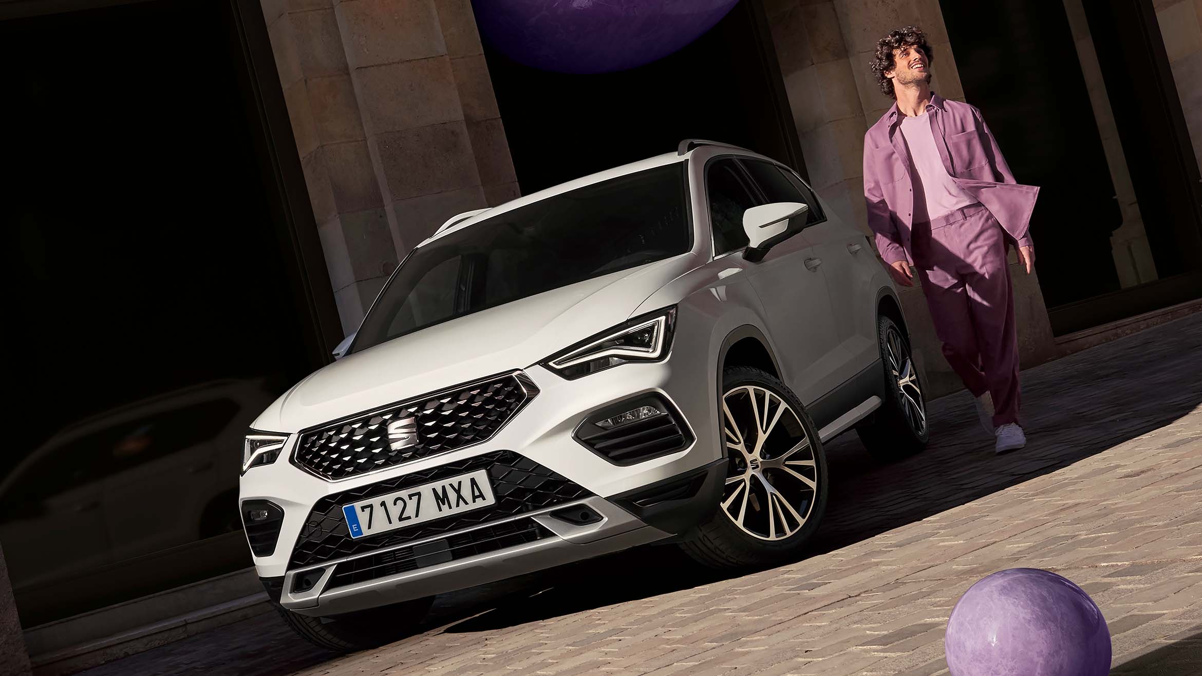 man standing by a 2024 seat ateca xperience car at dusk in a city arcade, frontal view of the car 