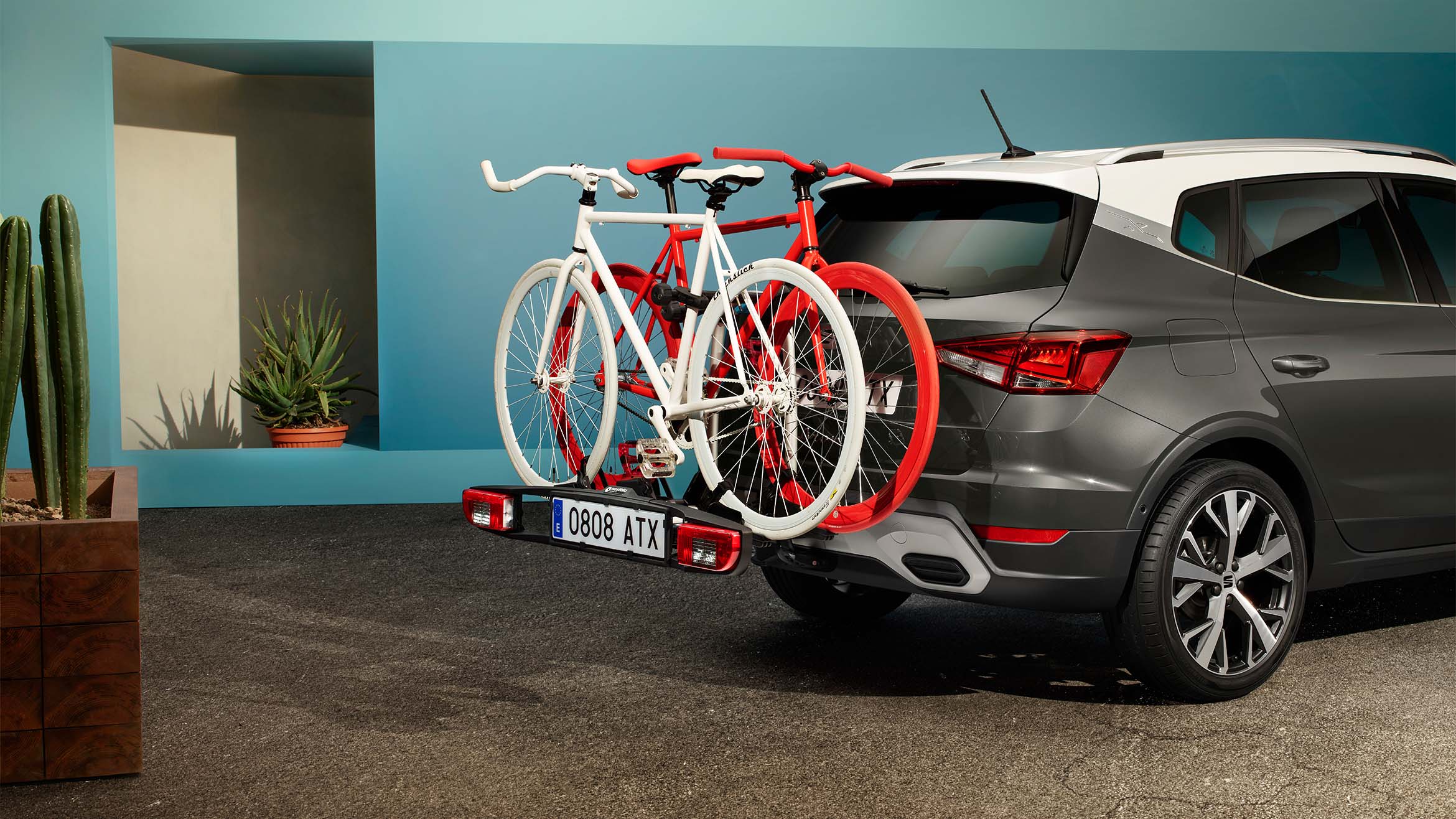 Rear view of a SEAT Arona in black with a white roof carrying two bikes in the towing bike rack. The car is parked in a colourful setting outdoors.