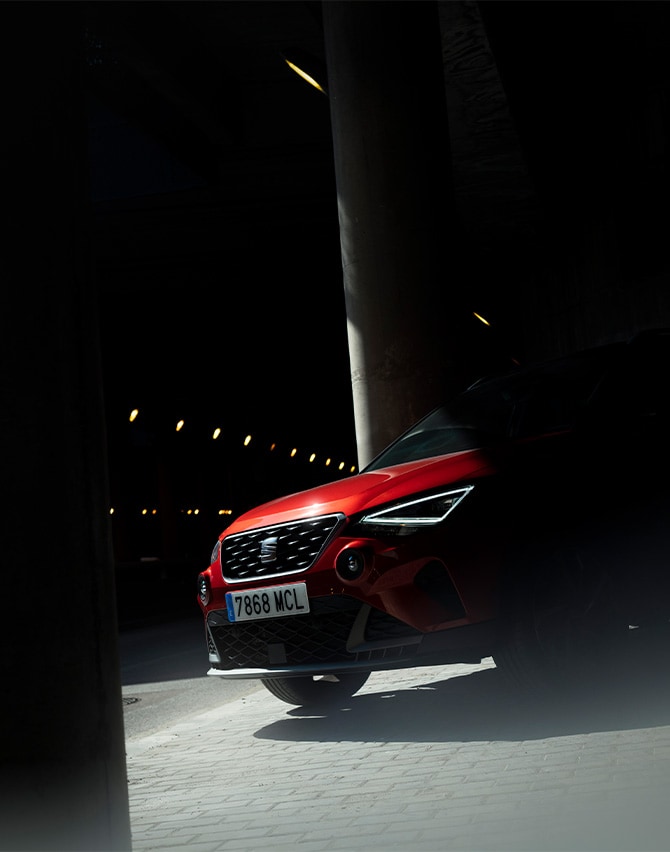 woman looking up and smiling next to a SEAT Arona in desire red color parked on the street