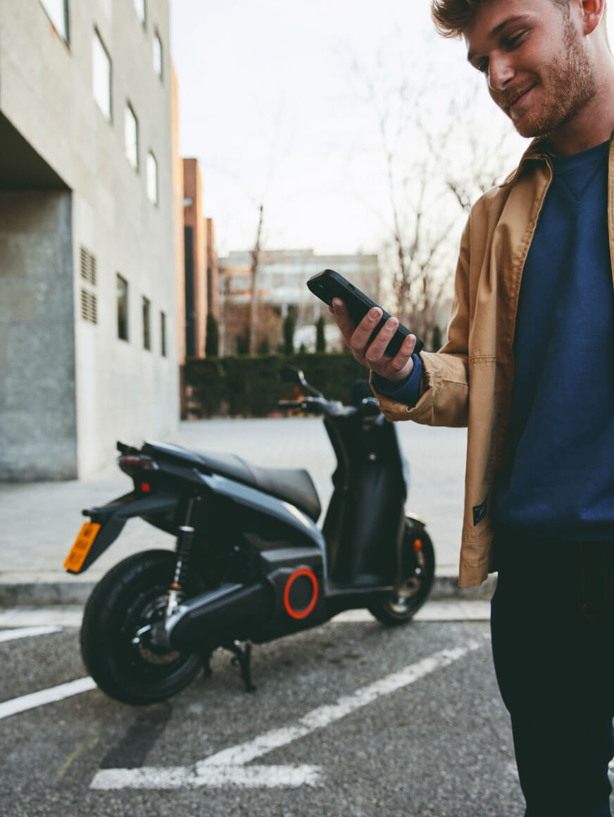 a man looking at his mobile with a SEAT MO 50 electric scooter behind