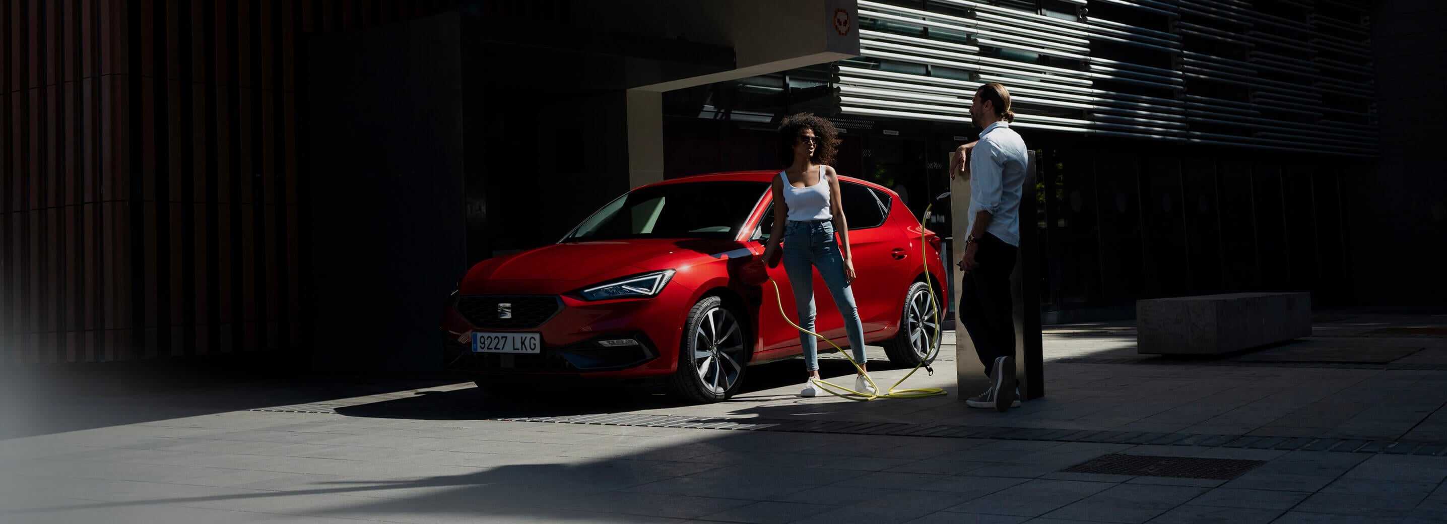 side view of a red desire Leon 5D plug in hybrid,being charged by a couple standing next to the car