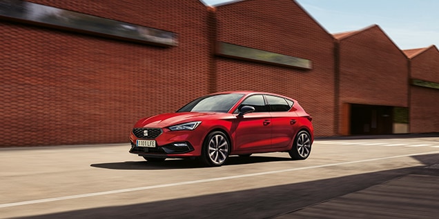 red seat leon driving in a restricted area, industrial brick buildings, showcasing its versatility and style