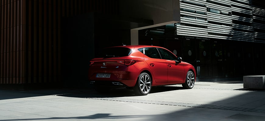 Mild hybrid electric vehicle seat leon sportstourer in red parked in the shadows by a building