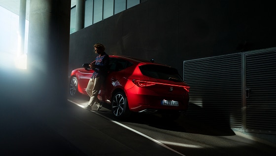 rear view of a red desire Leon 5D plug in hybrid,in an indoor parking, with a man leaning on the car