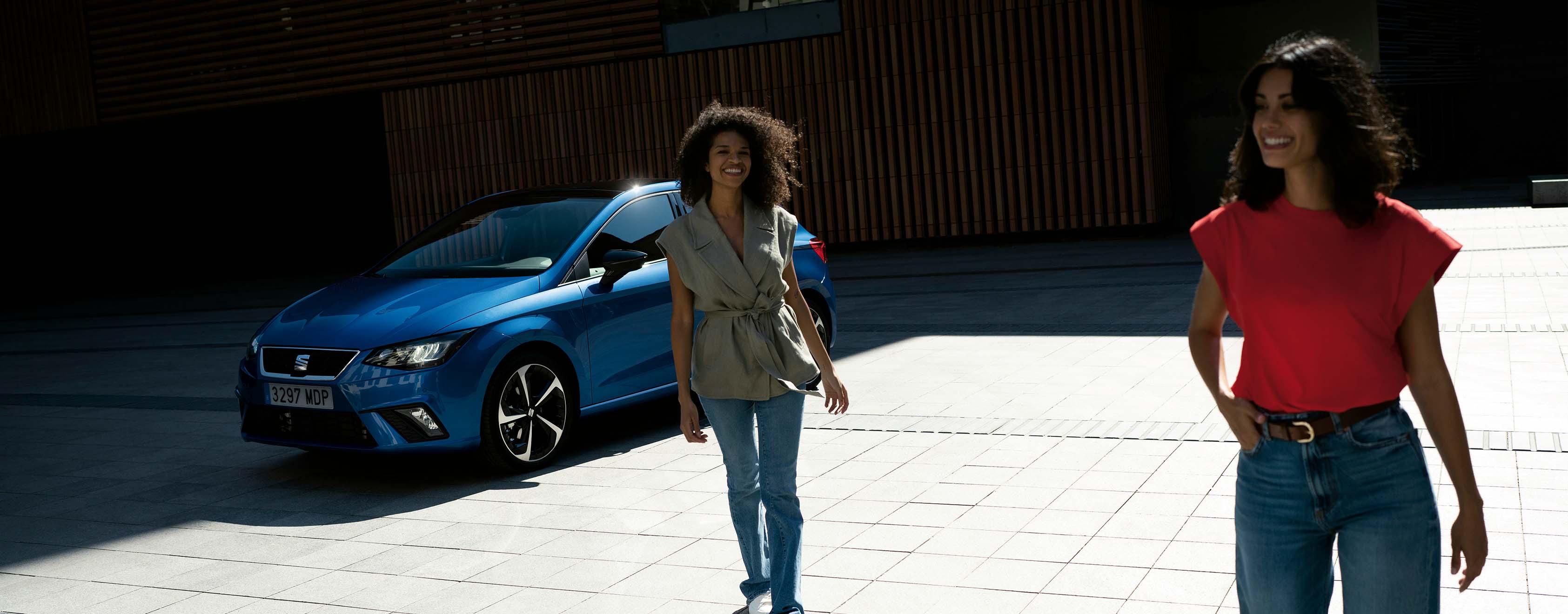 Seat ibiza in sapphire blue, two models walk in front of the vehicle smiling