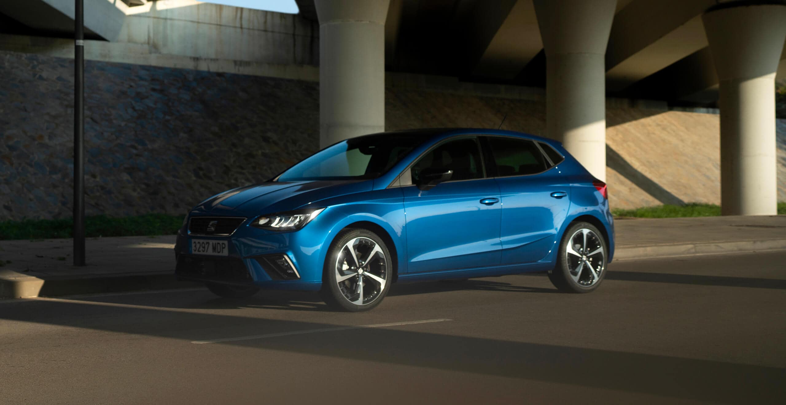 A side view of a blue Seat Ibiza, crossing under a bridge.