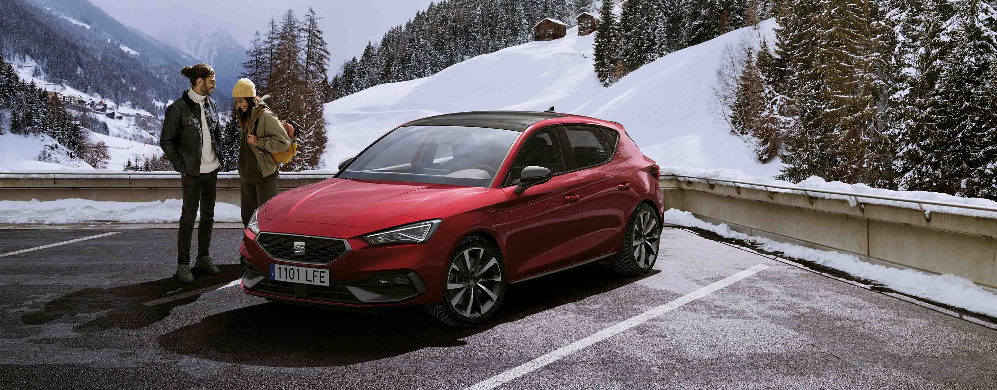 Seat leon in desire red on the road, models in a car park by the snow mountains and trees.