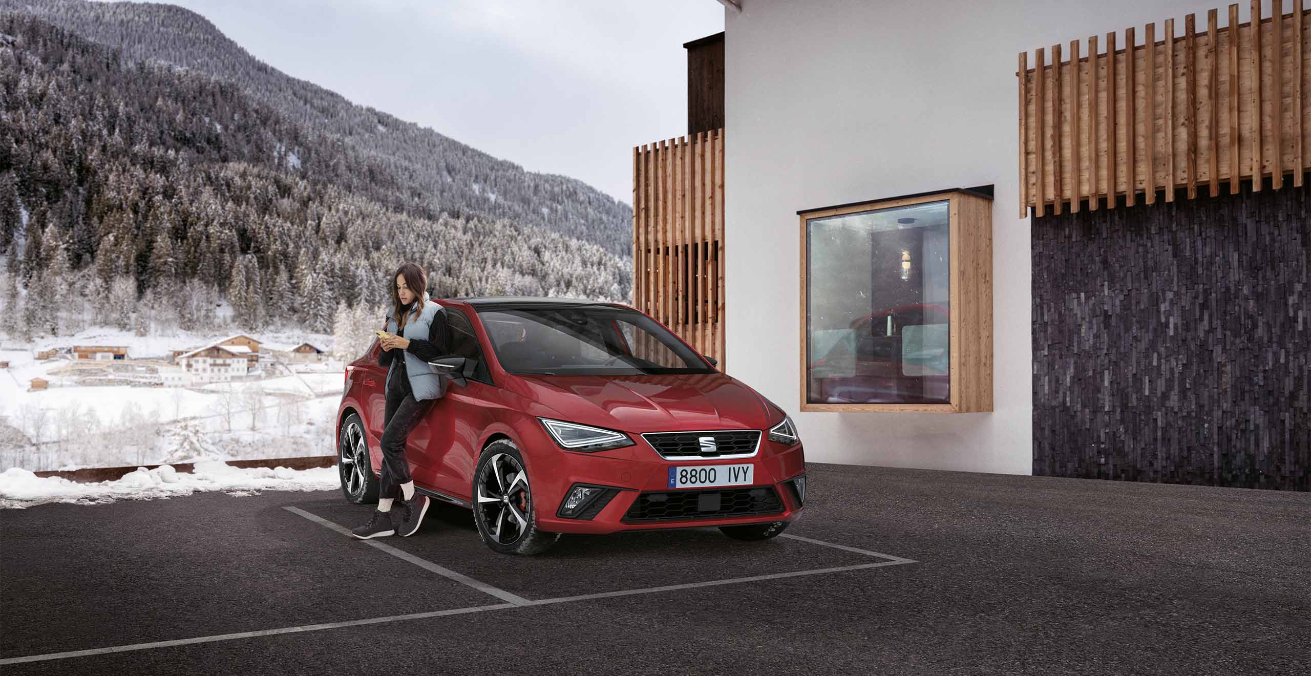 Seat ibiza awaiting car tyre service by white building with wooden panels, mountains in the background. 