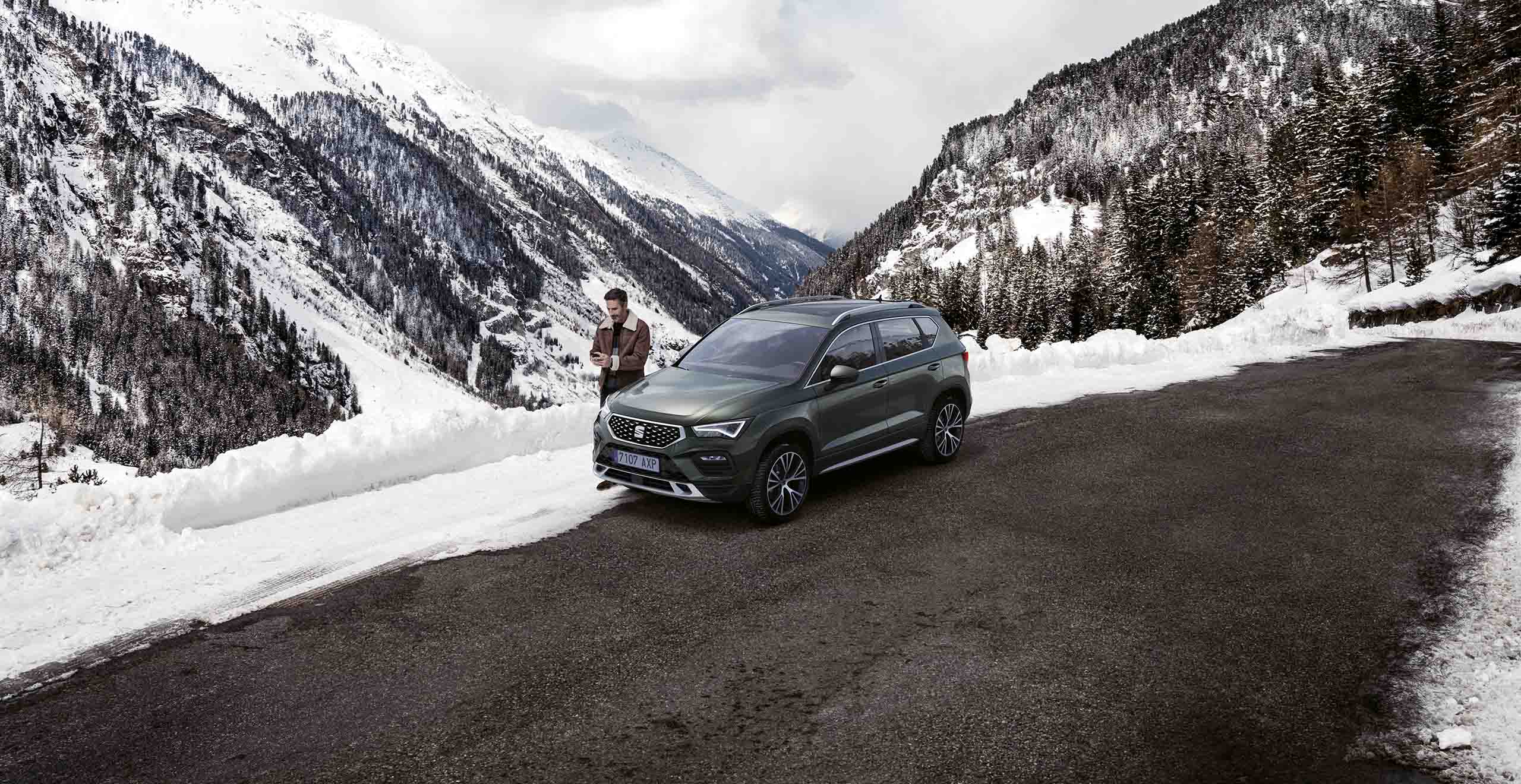 Seat ateca on the side of a road, awaiting roadside assistance on snowy mountain road during winter, showcasing its durability and performance in challenging weather conditions.